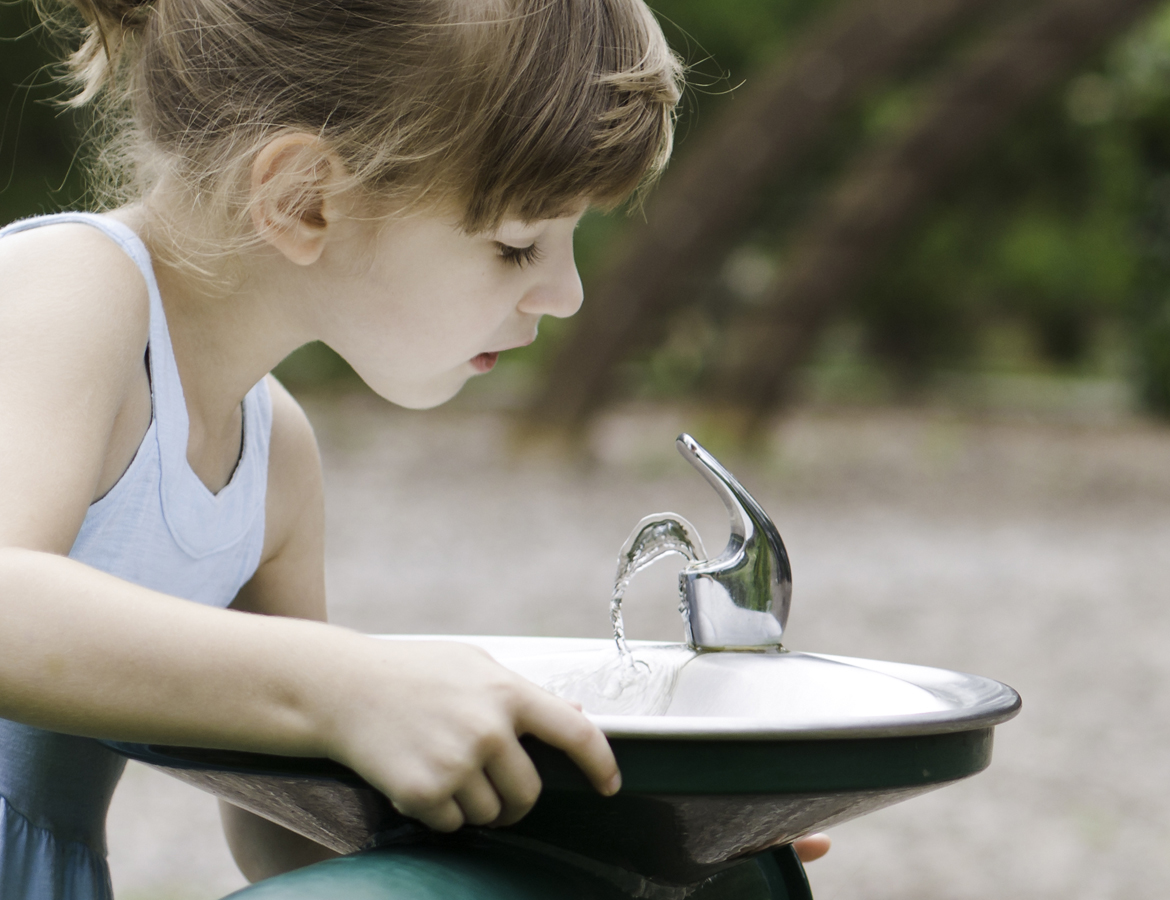 Young girl drinking from public water fountain