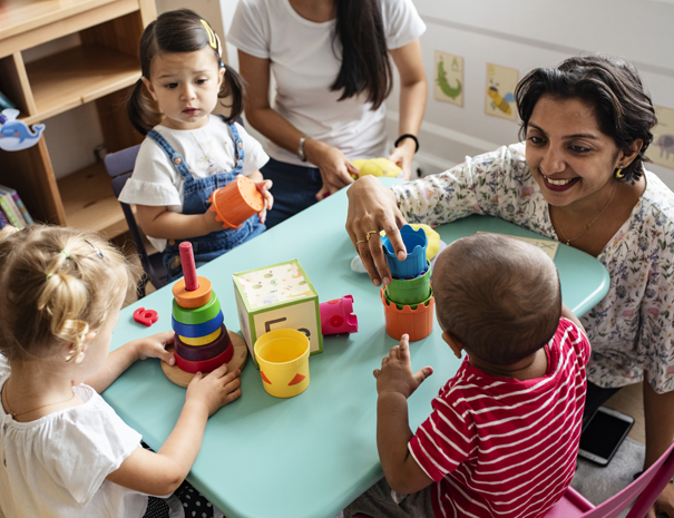 Day care teachers with toddlers around a table playing with toys